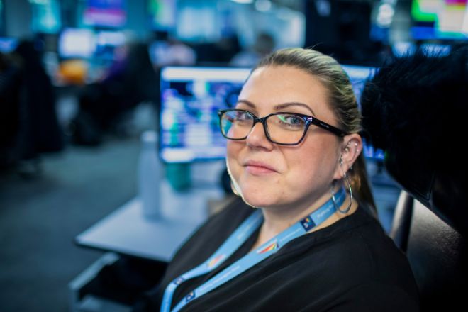 woman sat at her desk smiling with computers in the background